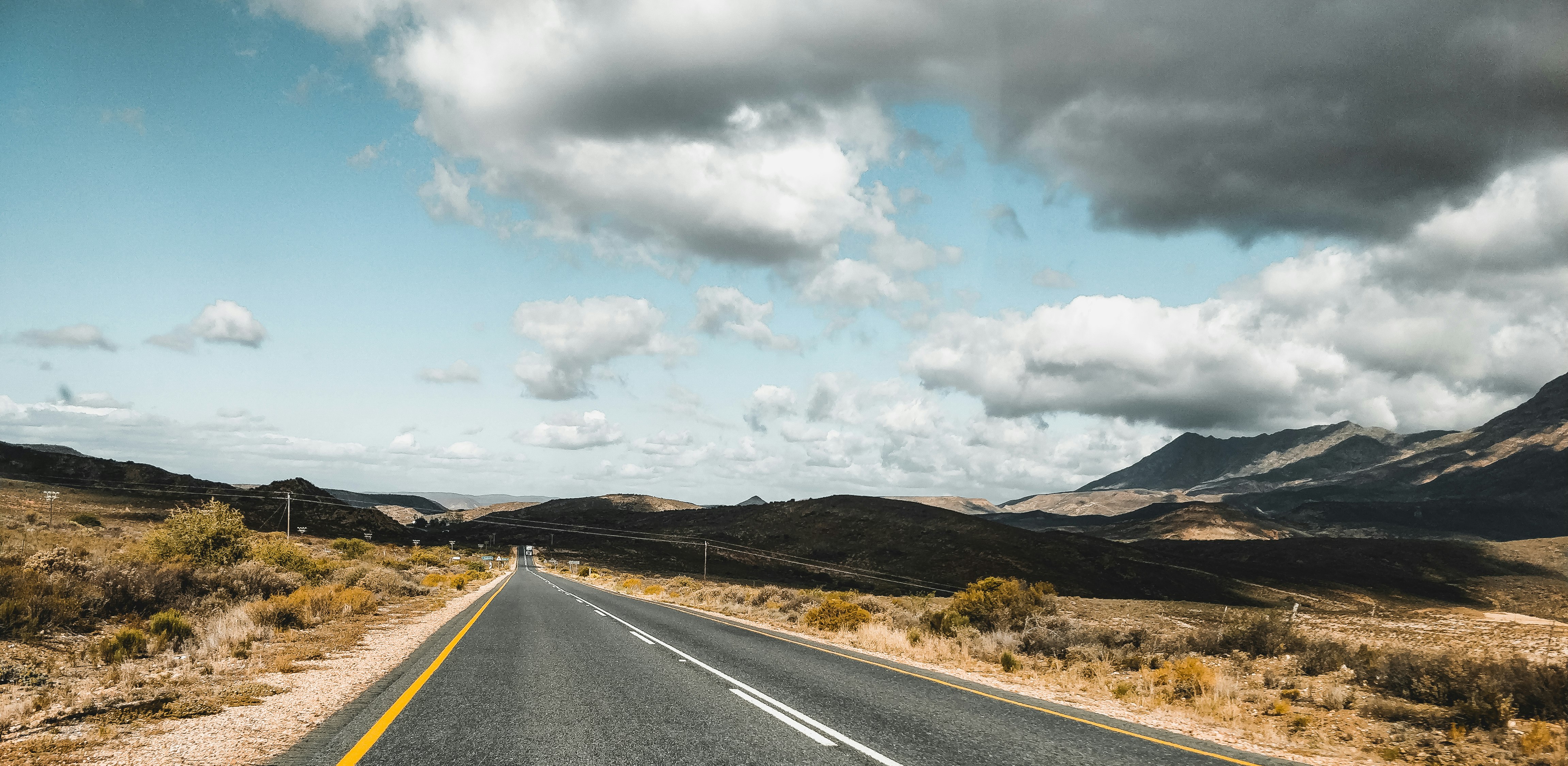 gray concrete road near brown mountain under white clouds during daytime